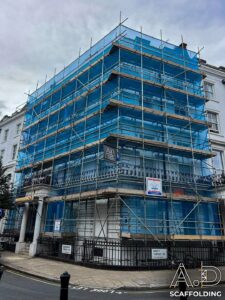 Scaffolding on corner building in London with blue safety netting in place & A.D. Scaffolding sign